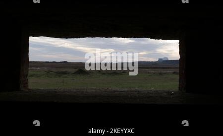 Das Kernkraftwerk Sizewell B wurde durch eine Lücke in einem Bunker (Pillbox) gesehen, der WW2 in den Ruinen von Leiston Chapel, Suffolk, Großbritannien, gebaut wurde Stockfoto