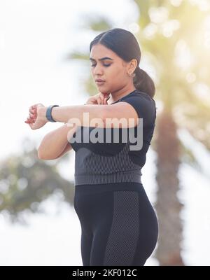 Junge Frau, Fitness und Herzfrequenz, Nackenpuls und Training plus Körpergröße in der Stadt. Sportlerin, Sportlerin und indisches Mädchen überprüfen Smart-Uhr Stockfoto