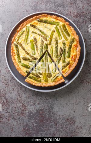 Spargel Cheese Pie eine leichte und kitschige Torte, die aus Eiern, Spargel und Zwiebeln in Nahaufnahme auf einem Teller auf dem Tisch zubereitet wird. Vertikale Draufsicht von oben Stockfoto