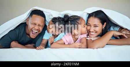 Schwarze Familie, Bett zusammen und glücklich unter Decke in zu Hause mit Liebe, Pflege und Bindung mit Kuss auf Wange. Schwarze Frau, Mann und Kinder im Schlafzimmer Stockfoto