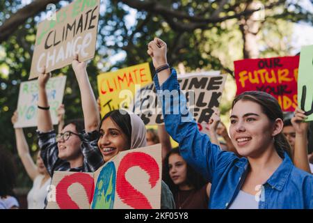 Fröhliche Jugendaktivisten erheben ihre Fäuste gegen den Klimawandel und die globale Erwärmung. Eine Gruppe verschiedener junger Menschen protestierte mit Plakaten und Spruchbändern Stockfoto