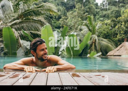 Porträt eines glücklichen jungen Mannes im Schwimmbad, der wegschaut. Kaukasischer Mann im Pool im Luxus-Urlaubsort. Stockfoto