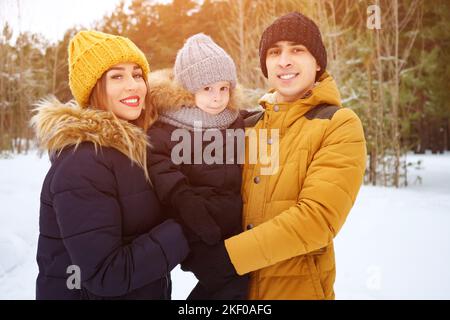 Mama und Papa kuscheln und küssen ihren kleinen Sohn im Winterpark. Stockfoto