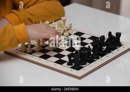 Sitzt an einem Tisch und spielt Schach. Das Kind konzentrierte sich auf das Spiel und überlegt, wo er seinen nächsten Schritt machen kann. Frühe Entwicklung, zu Hause pädagogische Spiele Stockfoto