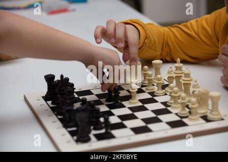 Sitzt an einem Tisch und spielt Schach. Das Kind konzentrierte sich auf das Spiel und überlegt, wo er seinen nächsten Schritt machen kann. Frühe Entwicklung, zu Hause pädagogische Spiele Stockfoto