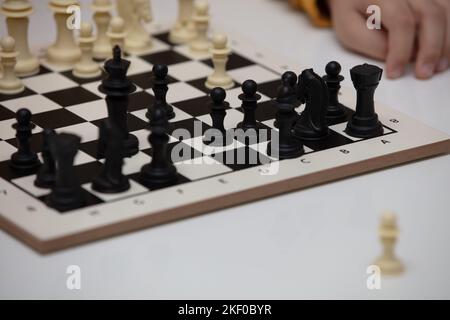 Sitzt an einem Tisch und spielt Schach. Das Kind konzentrierte sich auf das Spiel und überlegt, wo er seinen nächsten Schritt machen kann. Frühe Entwicklung, zu Hause pädagogische Spiele Stockfoto