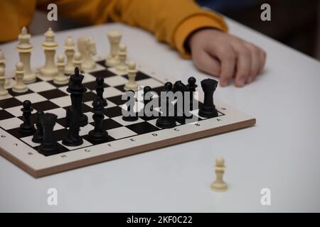 Sitzt an einem Tisch und spielt Schach. Das Kind konzentrierte sich auf das Spiel und überlegt, wo er seinen nächsten Schritt machen kann. Frühe Entwicklung, zu Hause pädagogische Spiele Stockfoto