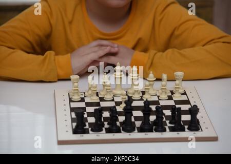 Sitzt an einem Tisch und spielt Schach. Das Kind konzentrierte sich auf das Spiel und überlegt, wo er seinen nächsten Schritt machen kann. Frühe Entwicklung, zu Hause pädagogische Spiele Stockfoto
