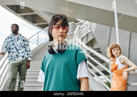 Eine vielfältige Gruppe junger Menschen, die Straßenkleidung im Freien tragen, konzentriert sich auf asiatische Männer mit Kopfhörern im Vordergrund Stockfoto