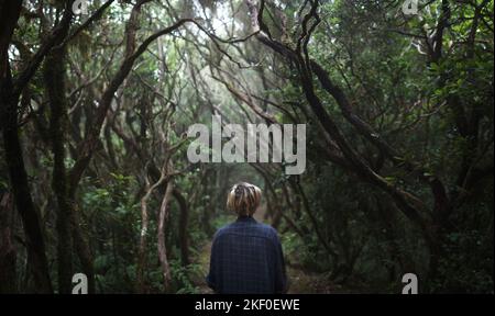 Eine junge Frau mit kurzen Haaren, die auf einem Pfad in einem dunklen Wald aus verdrehten Bäumen steht Stockfoto