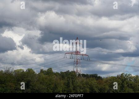 Rot-weißer Hochspannungspylon für die Übertragung von Elektrizität mit detaillierten Oberleitungen zwischen Bäumen im Wald. Stockfoto