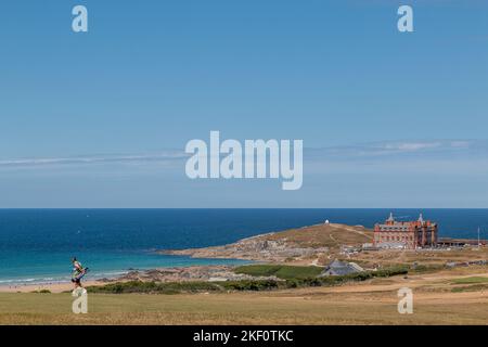 Ein Golfer spaziert entlang des Golfplatzes Newquay mit Blick auf den Fistral Beach und das Headland Cornwall Hotel. Stockfoto