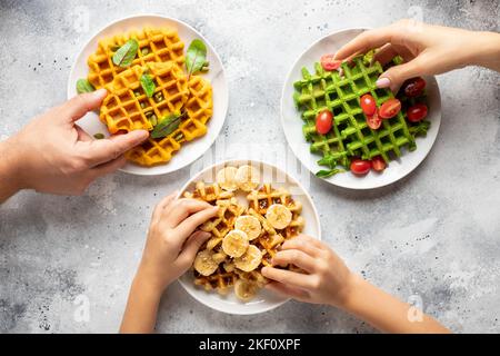 Glückliche Familie beim Frühstück. Eltern mit Kind essen verschiedene belgische Waffeln Stockfoto