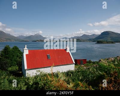 Ein rot überdachtes weiß gewaschenes Häuschen mit Blick auf Loch Shieldaig und die Torridon-Berglandschaft in Wester Ross, Schottland, Großbritannien Stockfoto