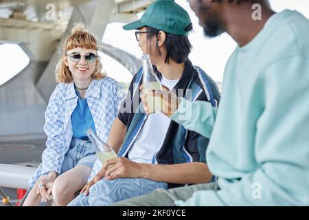 Eine vielfältige Gruppe junger Menschen, die sich im Freien in städtischer Umgebung aufhalten und Getränke genießen Stockfoto