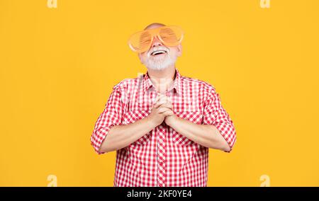 Betender älterer Mann mit Partybrille auf gelbem Hintergrund Stockfoto