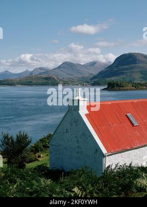 Ein rot überdachtes weiß gewaschenes Häuschen mit Blick auf Loch Shieldaig und die Torridon-Berglandschaft in Wester Ross, Schottland, Großbritannien Stockfoto