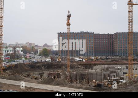 Die Baumaschinen befinden sich im Stadtzentrum in einer modernen Wohnanlage. Die Krane arbeiten. Die erste Phase des Baus eines mehrstöckigen Gebäudes im Stadtzentrum. Bau neuer Wohngebäude Stockfoto