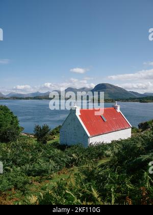 Ein rot überdachtes weiß gewaschenes Häuschen mit Blick auf Loch Shieldaig und die Torridon-Berglandschaft in Wester Ross, Schottland, Großbritannien Stockfoto