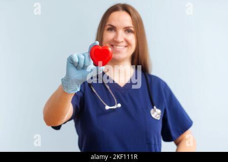 Ärztin mit Stethoskop, das rotes Herz auf blauem Hintergrund hält Stockfoto