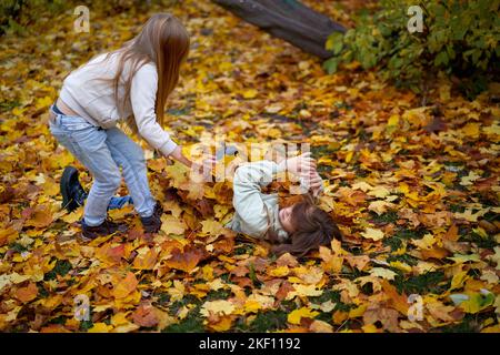 Kinder im Herbstpark liegen zwischen den bunten, hellen Ahornblättern und haben einen Ventilator. Herbstblätter fliegen herum. Kopieren Sie den Platz für Ihr Design. Stockfoto