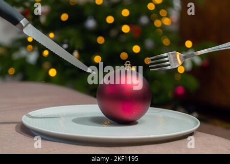 Weihnachts-Dinner-Idee, Ornament auf dem Tisch auf dem Teller. Verschwommenes Licht im Hintergrund, rotes Weihnachtszubehör auf dem Teller. Stockfoto
