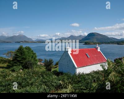 Ein rot überdachtes weiß gewaschenes Häuschen mit Blick auf Loch Shieldaig und die Torridon-Berglandschaft in Wester Ross, Schottland, Großbritannien Stockfoto