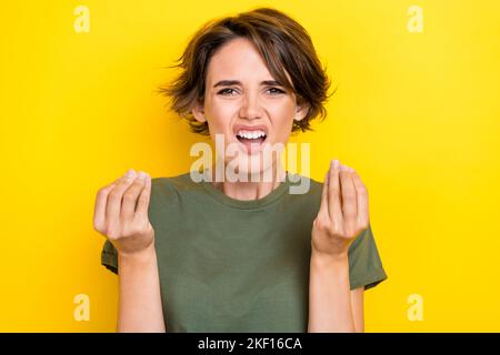 Foto von mädchenhaft unglücklich unzufrieden Mädchen mit bob Frisur tragen khaki T-Shirt Finger Gesicht Grimasse isoliert auf gelbem Hintergrund Stockfoto