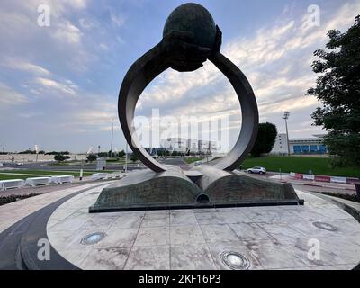 Hände, die aus einem Buch steigen, unterstützen die Welt in dieser Skulptur der Aspire Academy in Doha in Katar. Die 2022 Gebäude sind zwischen den Armen gerahmt. Stockfoto