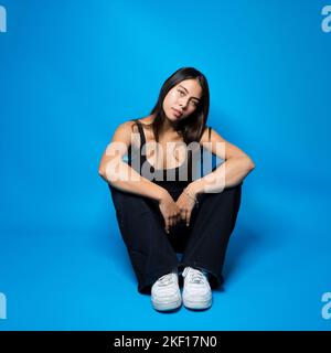 Multirassischer Teenager, der auf dem Boden in Fetalposition auf blauem Hintergrund mit Kopierraum sitzt Stockfoto