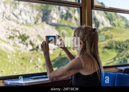 Reife Erwachsene weibliche Reisende mit Smartphone fotografieren Berge, während sie im Zug sitzen. Stockfoto