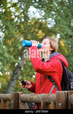 Wanderer, der aus einer Wasserflasche trinkt und die Aussicht auf den Wald betrachtet. Stockfoto