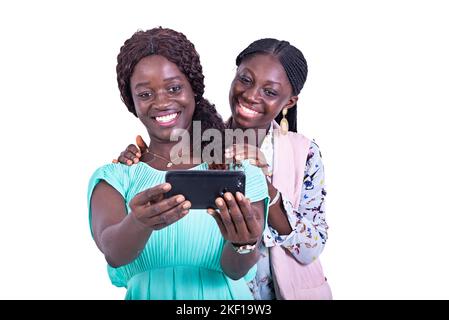 Porträt von zwei schönen glücklichen jungen Frauen, die Fotos auf dem Handy machen, während sie lächeln. Stockfoto