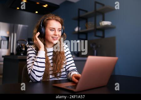 Customer Support Service Call Center Manager spricht, arbeitet von zu Hause aus. Lockige Frau mit Headset, spricht auf einer Videokonferenz mit einer Webcam am Laptop. Jung Stockfoto