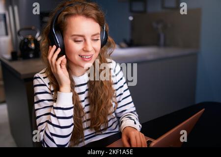 Customer Support Service Call Center Manager spricht, arbeitet von zu Hause aus. Lockige Frau mit Headset, spricht auf einer Videokonferenz mit einer Webcam am Laptop. Jung Stockfoto