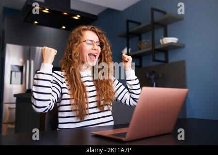 Glückliche Frau prüft E-Mails, gute Nachrichten über den Erfolg auf dem Laptop. Frau freut sich, feiert die Genehmigung des Visums, gewinnt Preis und Geld, Projektabschluss Stockfoto