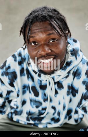 Vertikales Nahaufnahme-Porträt eines jungen schwarzen Mannes, der einen Hoodie trägt und die Kamera anlächelt Stockfoto