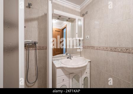 Badezimmer mit weißen Porzellanarmaturen, weißen Marmorablagen, eingebautem Spiegel und begehbarer Dusche Stockfoto