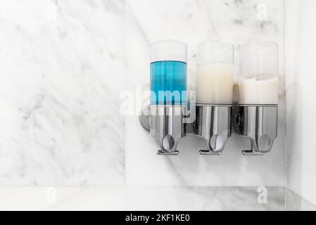 Spender für Seife, Shampoo und Weichspüler an der Wand einer Dusche mit weißem Marmor Stockfoto