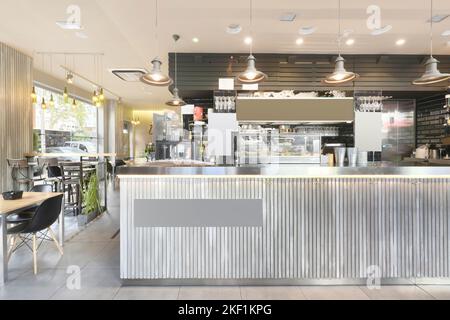 Lounge einer Cafeteria mit Holztischen und polierter Metallbar, Lampen und technischer Decke Stockfoto