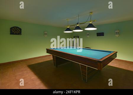 Billardtisch aus Holz in einem Raum mit grün gestrichenen Wänden und braunen Steinzeugböden Stockfoto