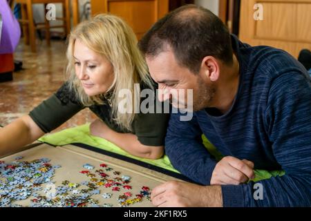Gebundenes Paar, das auf dem Boden liegt und ein Puzzle macht. Frau fühlt sich glücklich, Zeit als Paar zu verbringen, während Mann in Meinungsverschiedenheiten murmelte. Stockfoto
