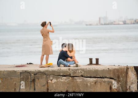 Eine Frau macht ein Foto eines jungen romantischen Paares auf der Tejo Promenade, Fluss Tejo Lissabon, Portugal. Dieser Flussweg entlang des Flusses in Lissabon Stockfoto