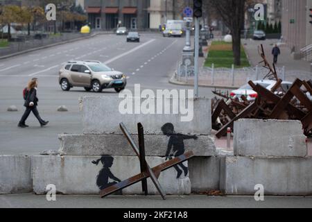 Kiew, Ukraine. 07.. November 2022. Ein Mädchen geht an einem Graffiti des britischen Graffiti-Künstlers Banksy vorbei, das Kinder auf einem Panzerabwehrigel wie eine Säge auf dem Unabhängigkeitsplatz in Kiew zeigt. Der weltberühmte anonyme Straßenkünstler Banksy besuchte die Ukraine im November 2022 und schuf 7 Graffiti in seinem unverkennbaren Stil. (Foto von Oleksii Chumachenko/SOPA Images/Sipa USA) Quelle: SIPA USA/Alamy Live News Stockfoto
