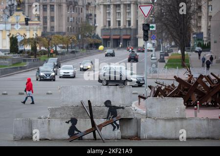 Kiew, Ukraine. 07.. November 2022. Eine Frau geht an einem Graffiti des britischen Graffiti-Künstlers Banksy vorbei, in dem Kinder auf einem Panzerabwehrigel wie eine Säge auf dem Unabhängigkeitsplatz in Kiew reiten. Der weltberühmte anonyme Straßenkünstler Banksy besuchte die Ukraine im November 2022 und schuf 7 Graffiti in seinem unverkennbaren Stil. (Foto von Oleksii Chumachenko/SOPA Images/Sipa USA) Quelle: SIPA USA/Alamy Live News Stockfoto