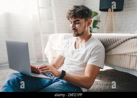 Ruhiger Mann, der sich mit einem Laptop auf dem Boden entspannt und faule Freizeit genießt. Genießen Sie die täglichen Aktivitäten in entspannter Atmosphäre. Genießen Sie den entspannenden Ruhestand Stockfoto