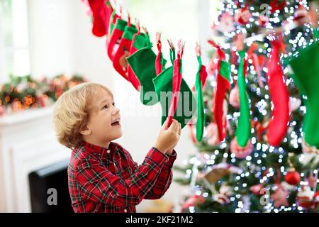 Kinder eröffnen Weihnachtsgeschenke. Kind auf der Suche nach Süßigkeiten und Geschenken im Adventskalender am Wintermorgen. Geschmückter Weihnachtsbaum Stockfoto