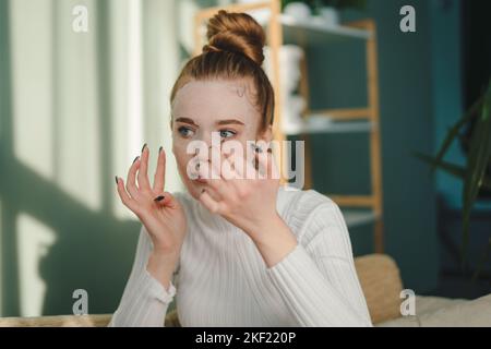 Schöne junge Dame, die auf der Couch sitzt, ihre Schönheitskur genießt und eine weiße Gesichtsmaske aufsetzt. Schönheitsbehandlung. Natürliche Schönheit. Frau Stockfoto