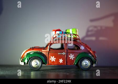 Ein kleines rotes Neujahrsauto im Retro-Stil mit Geschenken auf dem Dach. Stockfoto