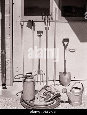 1940S GRUPPE GARTENGERÄTE HACKE SPATEN RECHEN GIESSKANNE LEHNT SICH AN GARAGENTOR - G3512 HAR001 HARS ALTMODISCH Stockfoto